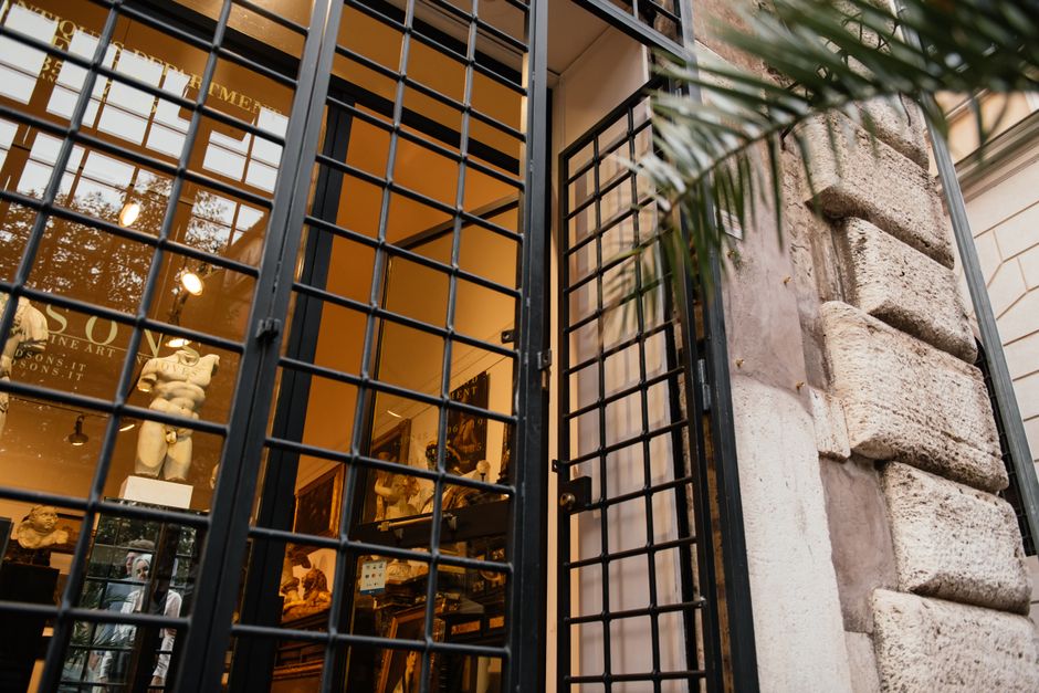 Low angle view of a historic building entrance with iron gates revealing classical sculptures inside.