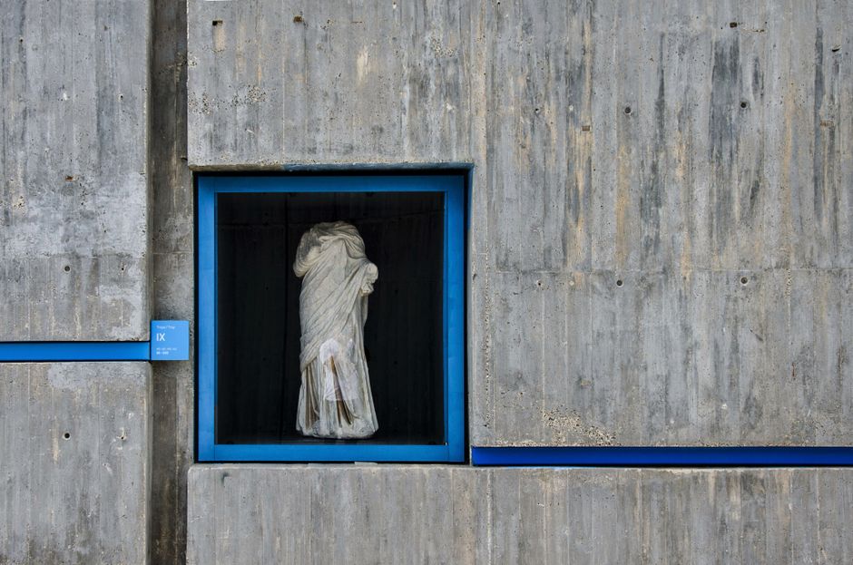 A classical statue encased in a modern concrete structure, highlighting contrast in design.