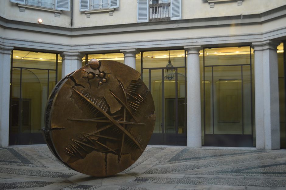 A bronze sculpture with abstract design in an urban courtyard setting.